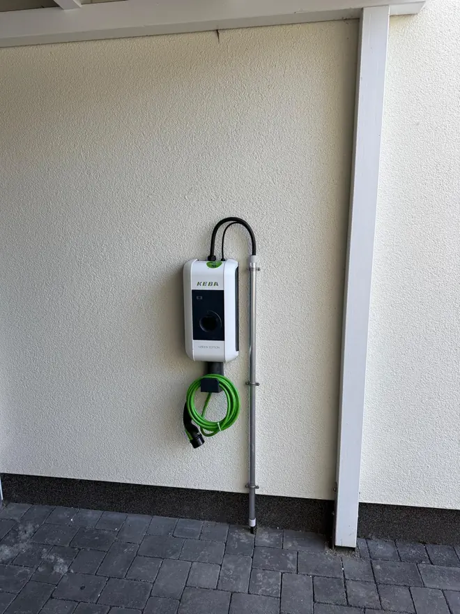 Wandmontierte Wallbox mit aufgehängtem Ladekabel an der Fassade eines Einfamilienhauses