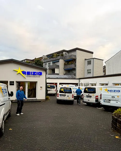 Mitarbeiter von REIZIG auf dem Betriebshof in Köln zwischen den beschrifteten Servicefahrzeugen
